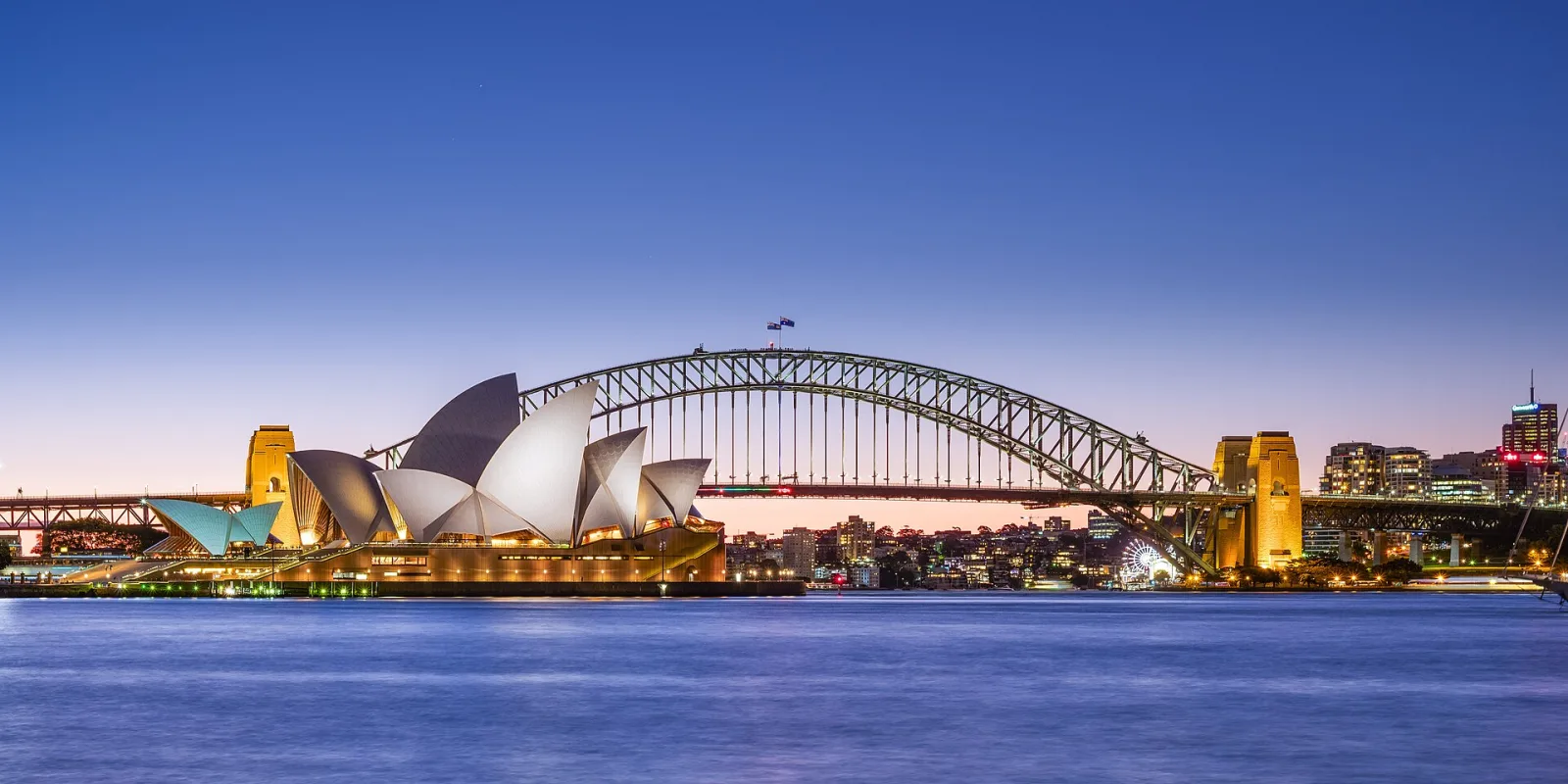 Jørn Utzon's Sydney Opera House, and the Harbour Bridge, two of Sydney's most famous landmarks, taken at late dusk. The Sydney Opera House is one of the most iconic buildings built in the 20th century (1973) and is UNESCO's world heritage.